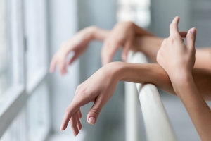 The hands of two classic ballet dancers at ballet barre on a  white room background
